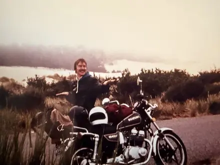 Robert astride a motorcycle on the Oregon Coast, hills behind him.