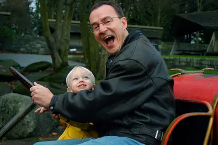 Robert throwing his head back laughing beside his great-nephew Noah, who is gripping a play-structure lever.