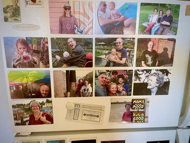 Robert&rsquo;s own refrigerator door, covered edge to edge with family photographs in magnetic frames, ticket stubs, and a magnet reading Mom&rsquo;s Mood is Good.